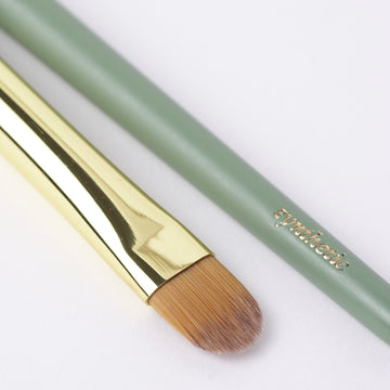 Flat concealer and cream eyeshadow brush with gold ferrule and sage green handle for detailed application.